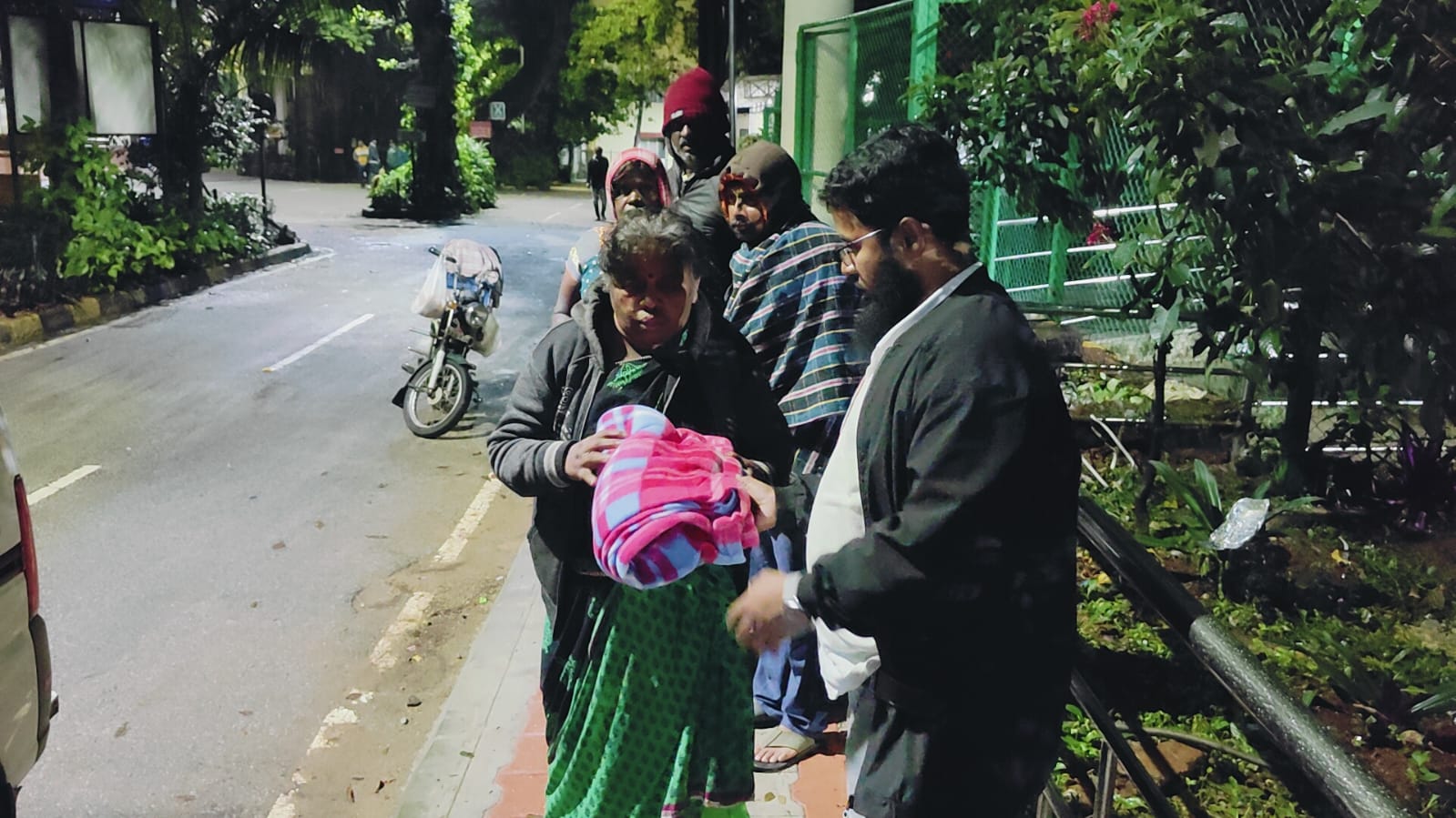A volunteer handing a blanket to a woman on the street at night