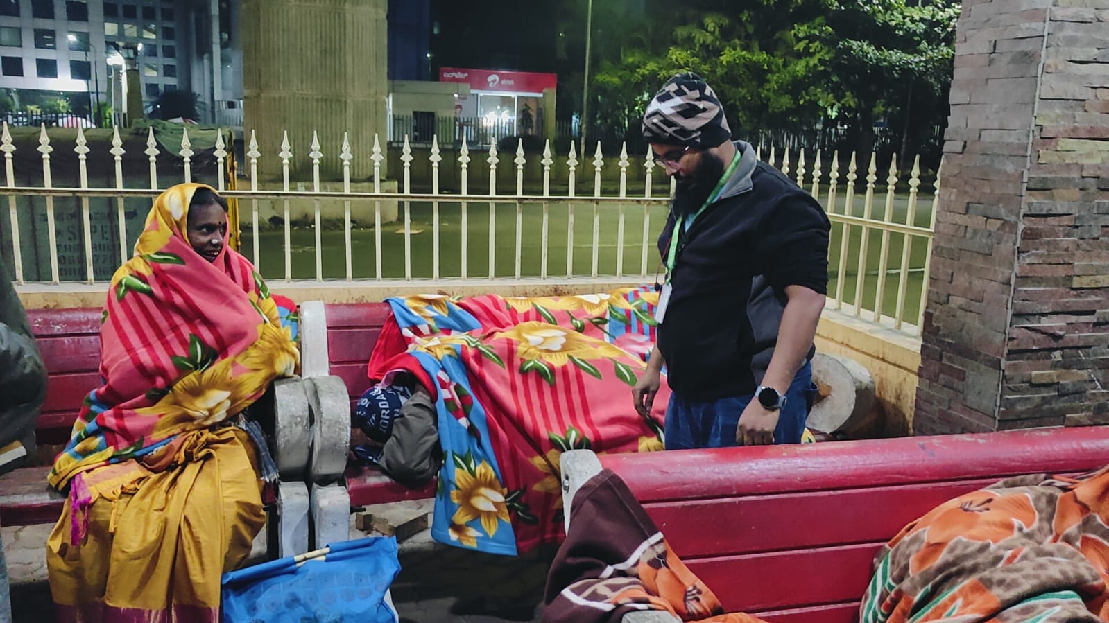 A volunteer covering people sleeping on benches with blankets at night